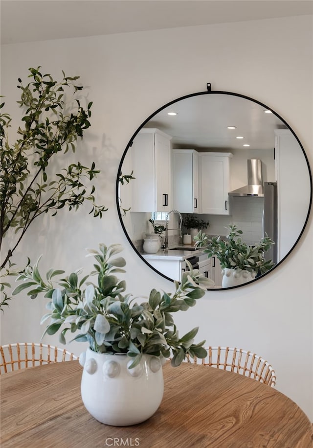 details featuring tasteful backsplash, wall chimney range hood, sink, stainless steel refrigerator, and white cabinets