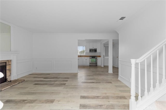 unfurnished living room with ornamental molding, light hardwood / wood-style floors, and a stone fireplace