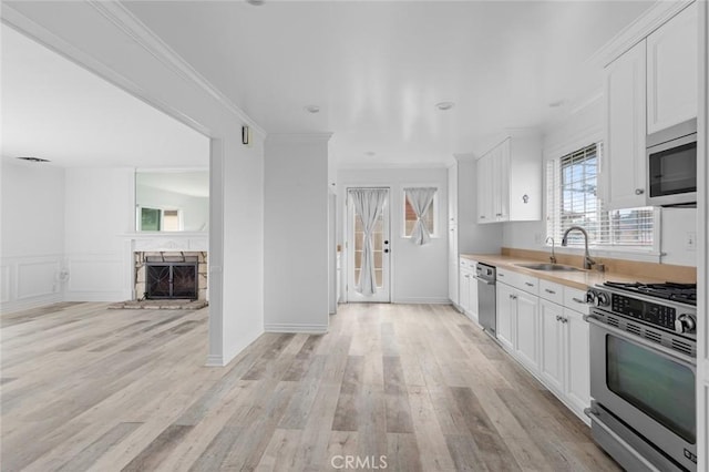 kitchen with appliances with stainless steel finishes, light wood-type flooring, crown molding, white cabinets, and sink