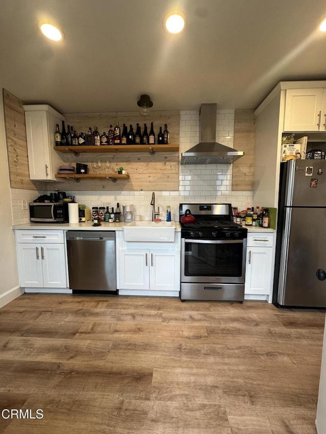 kitchen with wall chimney range hood, light hardwood / wood-style floors, sink, appliances with stainless steel finishes, and white cabinets