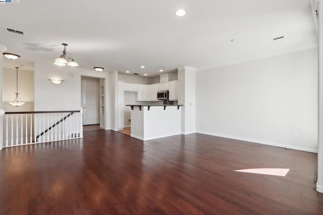 unfurnished living room with dark wood-type flooring, crown molding, and a chandelier