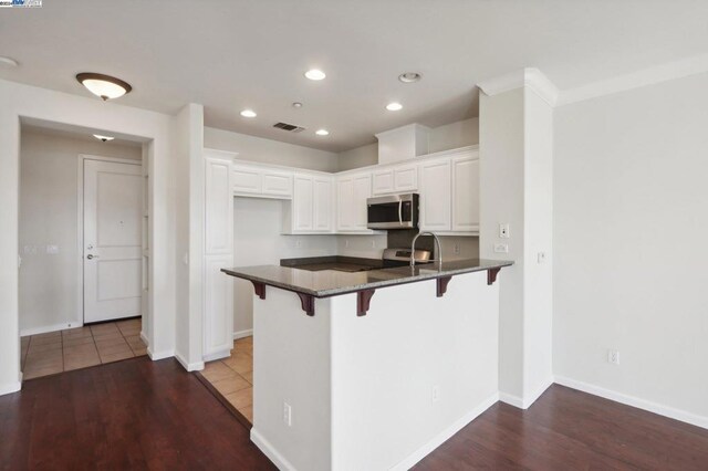 kitchen with white cabinetry, kitchen peninsula, hardwood / wood-style floors, appliances with stainless steel finishes, and a kitchen breakfast bar