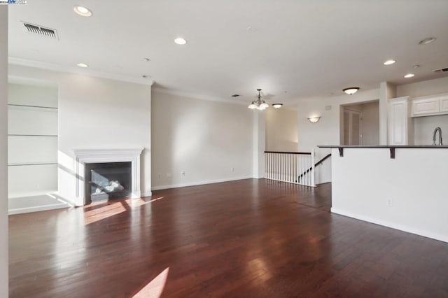 unfurnished living room with dark hardwood / wood-style floors, ornamental molding, and an inviting chandelier