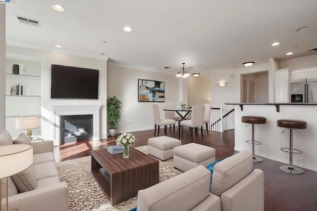 living room with wood-type flooring, built in features, crown molding, and a notable chandelier