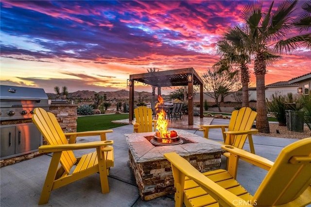 patio terrace at dusk with area for grilling, an outdoor fire pit, a mountain view, grilling area, and a pergola