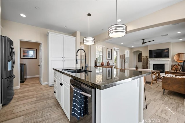 kitchen with an island with sink, black refrigerator with ice dispenser, pendant lighting, stainless steel dishwasher, and sink