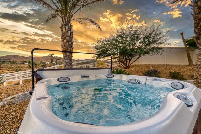 pool at dusk featuring a mountain view and a hot tub