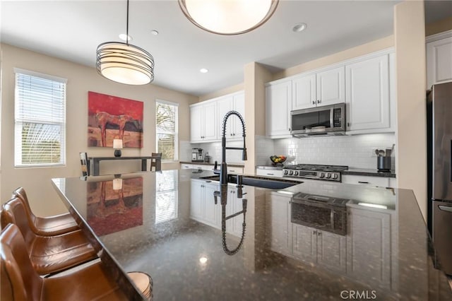 kitchen with pendant lighting, white cabinets, stainless steel appliances, sink, and backsplash