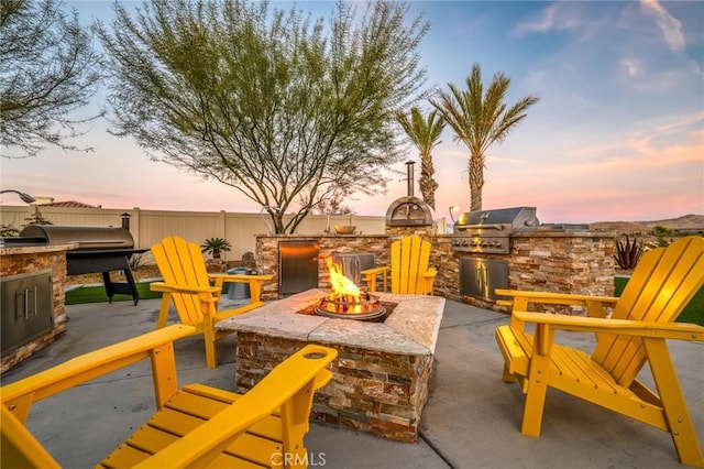 patio terrace at dusk featuring a grill, area for grilling, and an outdoor fire pit