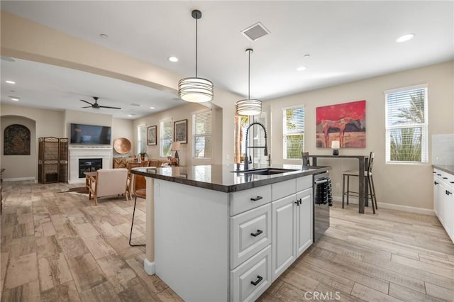 kitchen featuring a kitchen bar, an island with sink, ceiling fan, white cabinets, and sink