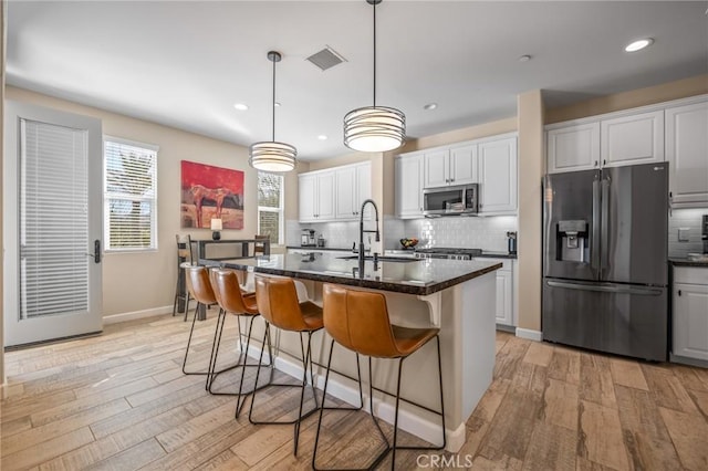 kitchen with refrigerator with ice dispenser, sink, white cabinetry, and a center island with sink