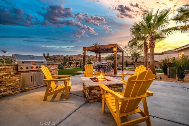 patio terrace at dusk featuring a grill, a mountain view, a fire pit, area for grilling, and a pergola