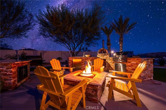 patio at twilight with an outdoor fire pit, a grill, and an outdoor kitchen