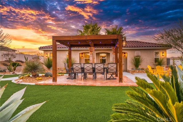 back house at dusk featuring a lawn and a patio