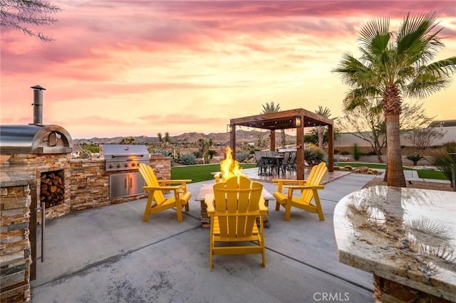 patio terrace at dusk featuring a mountain view, an outdoor fire pit, a grill, and area for grilling