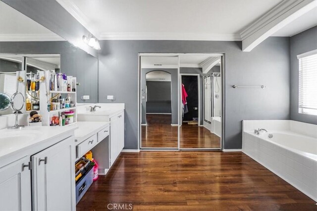 bathroom with tiled bath, vanity, wood-type flooring, and ornamental molding