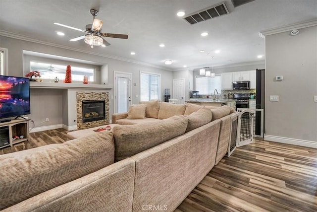 living room featuring ceiling fan, crown molding, hardwood / wood-style floors, and a stone fireplace