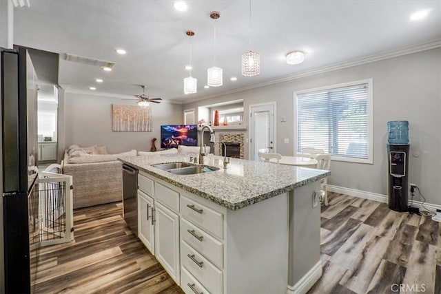 kitchen with decorative light fixtures, dishwasher, light stone countertops, an island with sink, and white cabinets