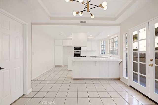 kitchen with white cabinets, kitchen peninsula, light tile patterned floors, and a tray ceiling