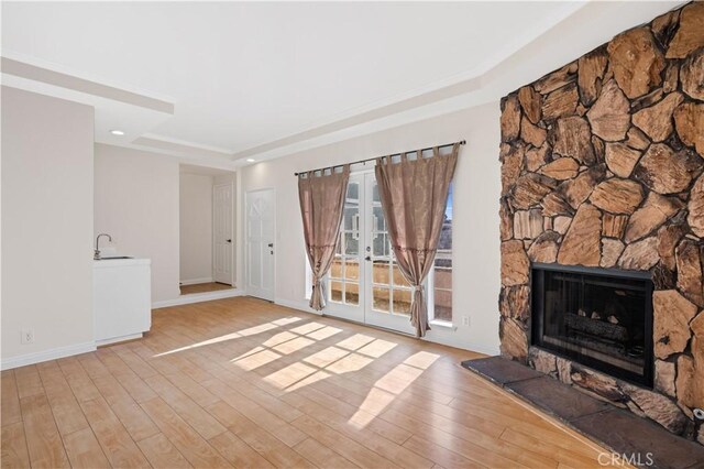 unfurnished living room with light hardwood / wood-style flooring, a tray ceiling, french doors, and a stone fireplace