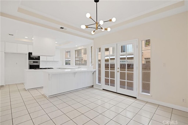 kitchen featuring white cabinets, hanging light fixtures, kitchen peninsula, a raised ceiling, and oven