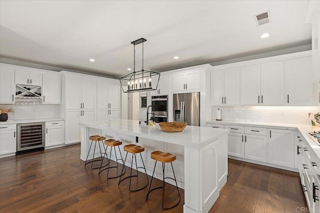 kitchen with white cabinetry, beverage cooler, appliances with stainless steel finishes, and a center island with sink