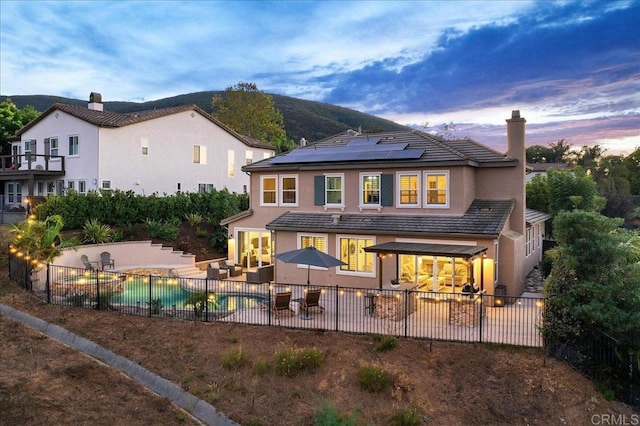 back house at dusk with an outdoor hangout area, a fenced in pool, solar panels, and a patio