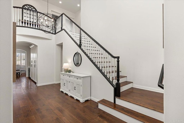 staircase featuring wood-type flooring, a notable chandelier, and a high ceiling