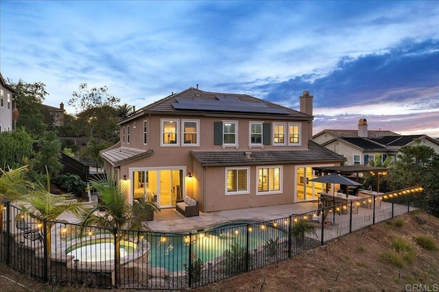 back house at dusk featuring a fenced in pool, solar panels, and a patio