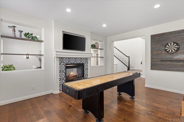 game room featuring built in shelves, a tiled fireplace, and dark wood-type flooring