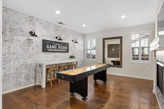 recreation room featuring a fireplace, a wealth of natural light, dark wood-type flooring, and brick wall