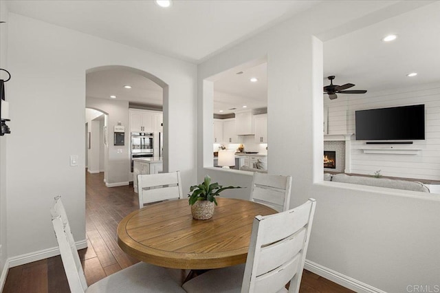 dining area featuring ceiling fan, dark wood-type flooring, and a fireplace