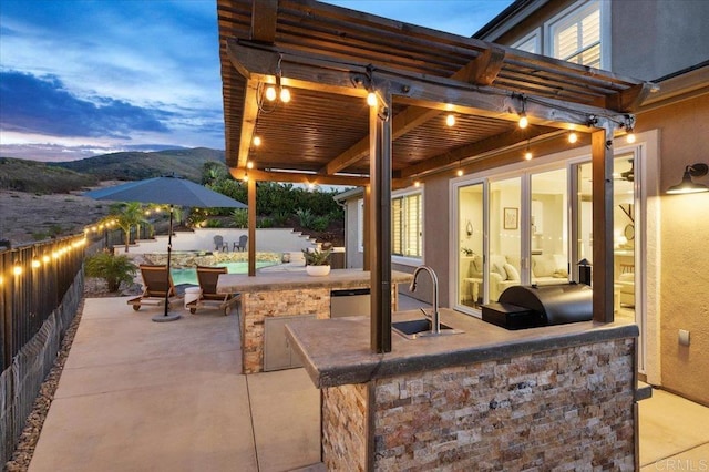 patio terrace at dusk featuring area for grilling, a mountain view, and an outdoor wet bar