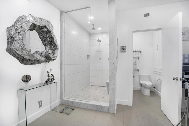 bathroom featuring toilet, a tile shower, and tile patterned flooring