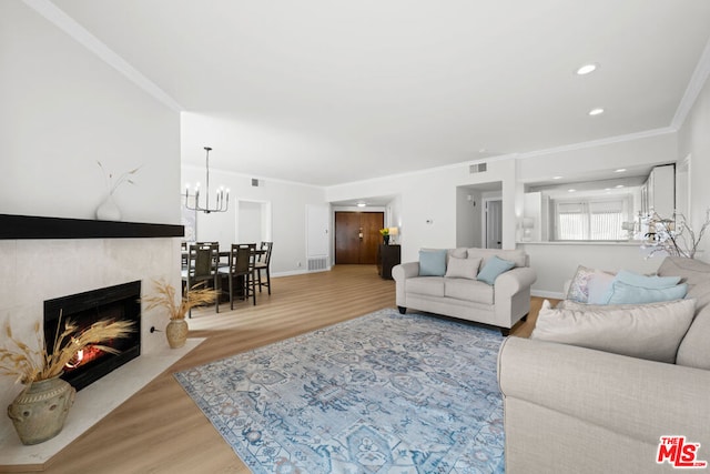 living room with hardwood / wood-style floors, ornamental molding, a premium fireplace, and an inviting chandelier