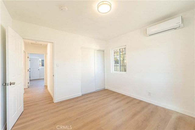 unfurnished bedroom with light wood-type flooring, a closet, and a wall unit AC