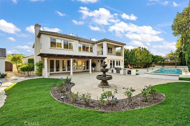 back of house featuring a balcony, an outdoor kitchen, a yard, a fenced in pool, and a patio area