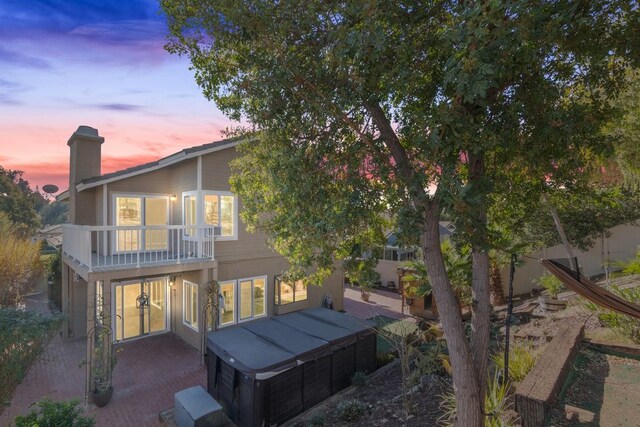 back house at dusk featuring a balcony and a patio