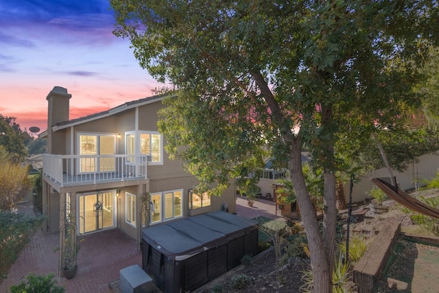 back house at dusk with a balcony and a patio