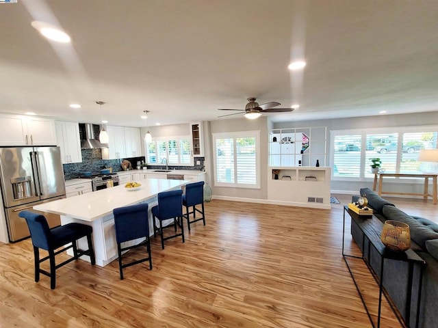 kitchen featuring white cabinetry, hanging light fixtures, a healthy amount of sunlight, stainless steel appliances, and wall chimney exhaust hood