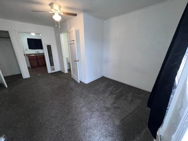 unfurnished bedroom featuring ceiling fan, ensuite bathroom, dark colored carpet, and sink