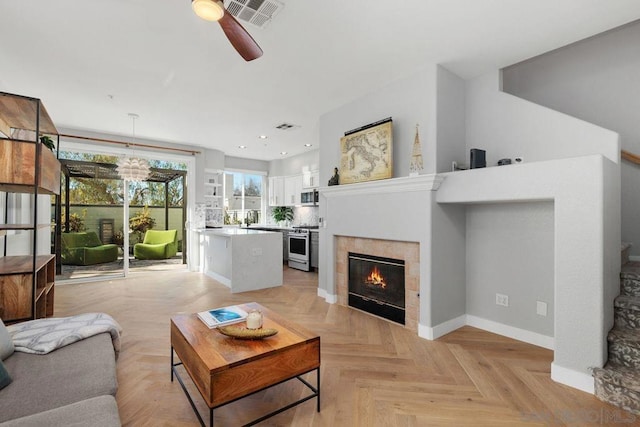 living room featuring light parquet floors, a tiled fireplace, and ceiling fan