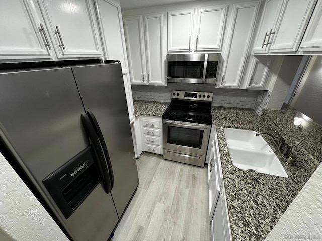 kitchen with stainless steel appliances, dark stone countertops, white cabinetry, and sink