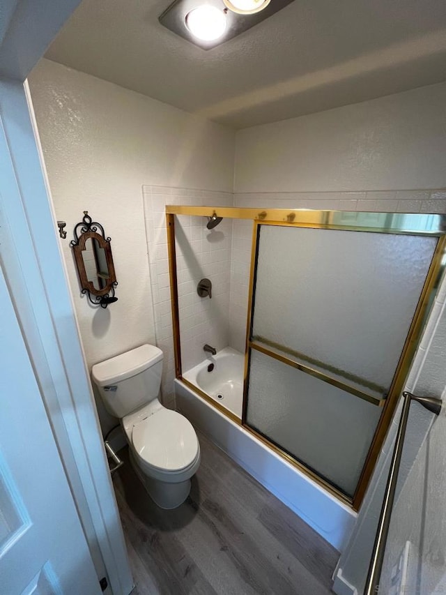 bathroom featuring hardwood / wood-style flooring, combined bath / shower with glass door, and toilet