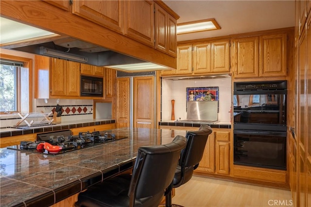 kitchen with decorative backsplash, a breakfast bar, black appliances, and light hardwood / wood-style flooring