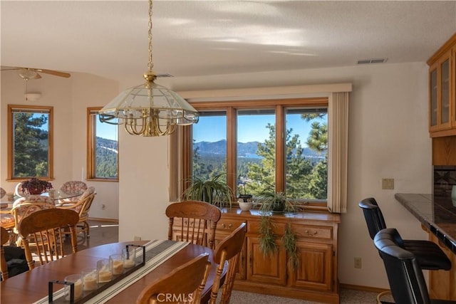 dining room with light carpet, ceiling fan with notable chandelier, and a mountain view