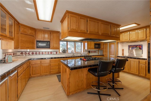 kitchen with tile counters, black microwave, a breakfast bar area, and a kitchen island