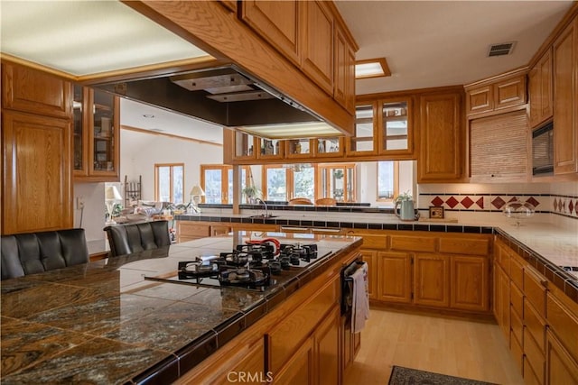 kitchen featuring exhaust hood, light hardwood / wood-style floors, kitchen peninsula, stainless steel gas cooktop, and sink