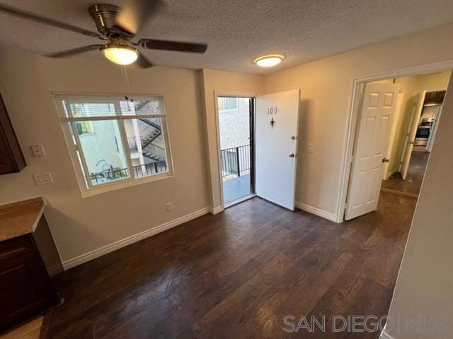 unfurnished dining area featuring ceiling fan, a textured ceiling, and dark hardwood / wood-style flooring