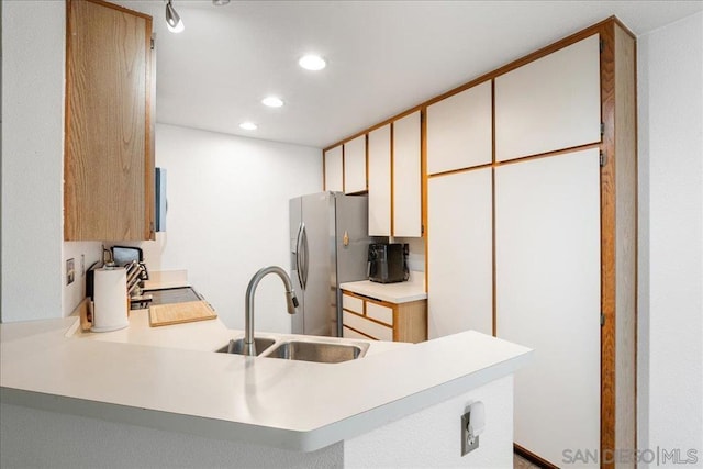 kitchen with kitchen peninsula, stainless steel refrigerator with ice dispenser, sink, white cabinets, and range